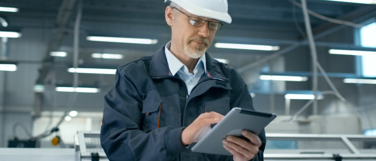 Senior engineer in hardhat is using a tablet computer in a factory.