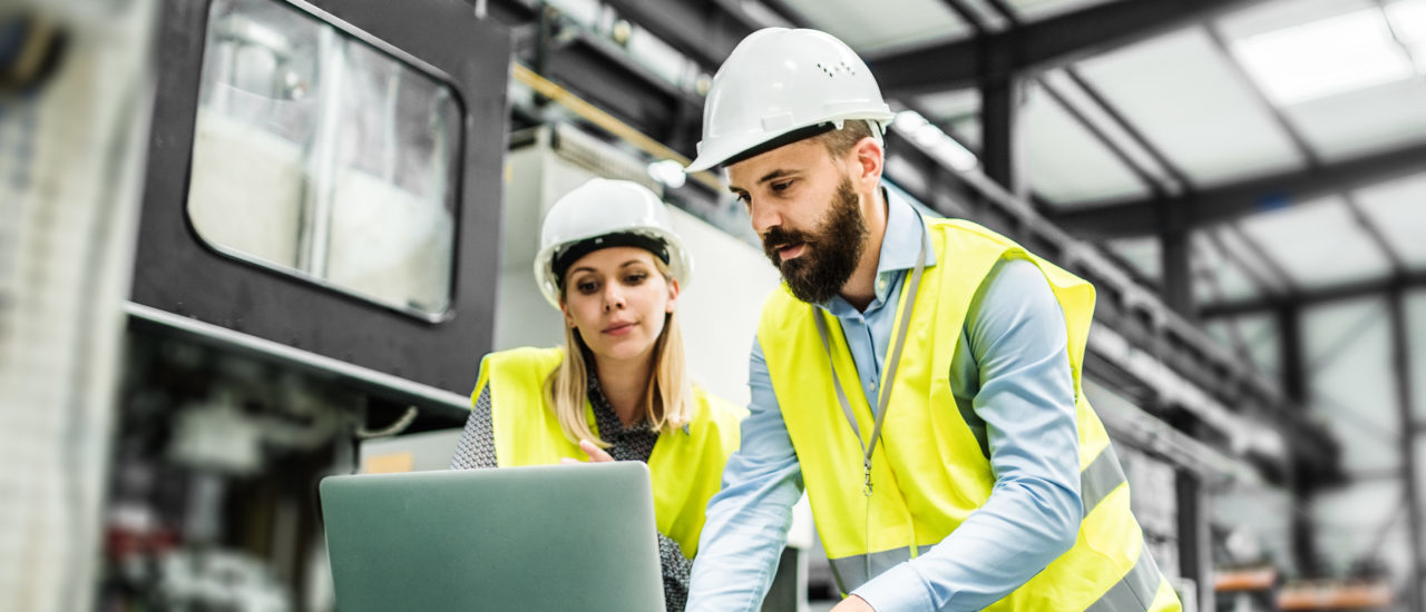 A portrait of an industrial man and woman engineer with laptop in a factory, working.